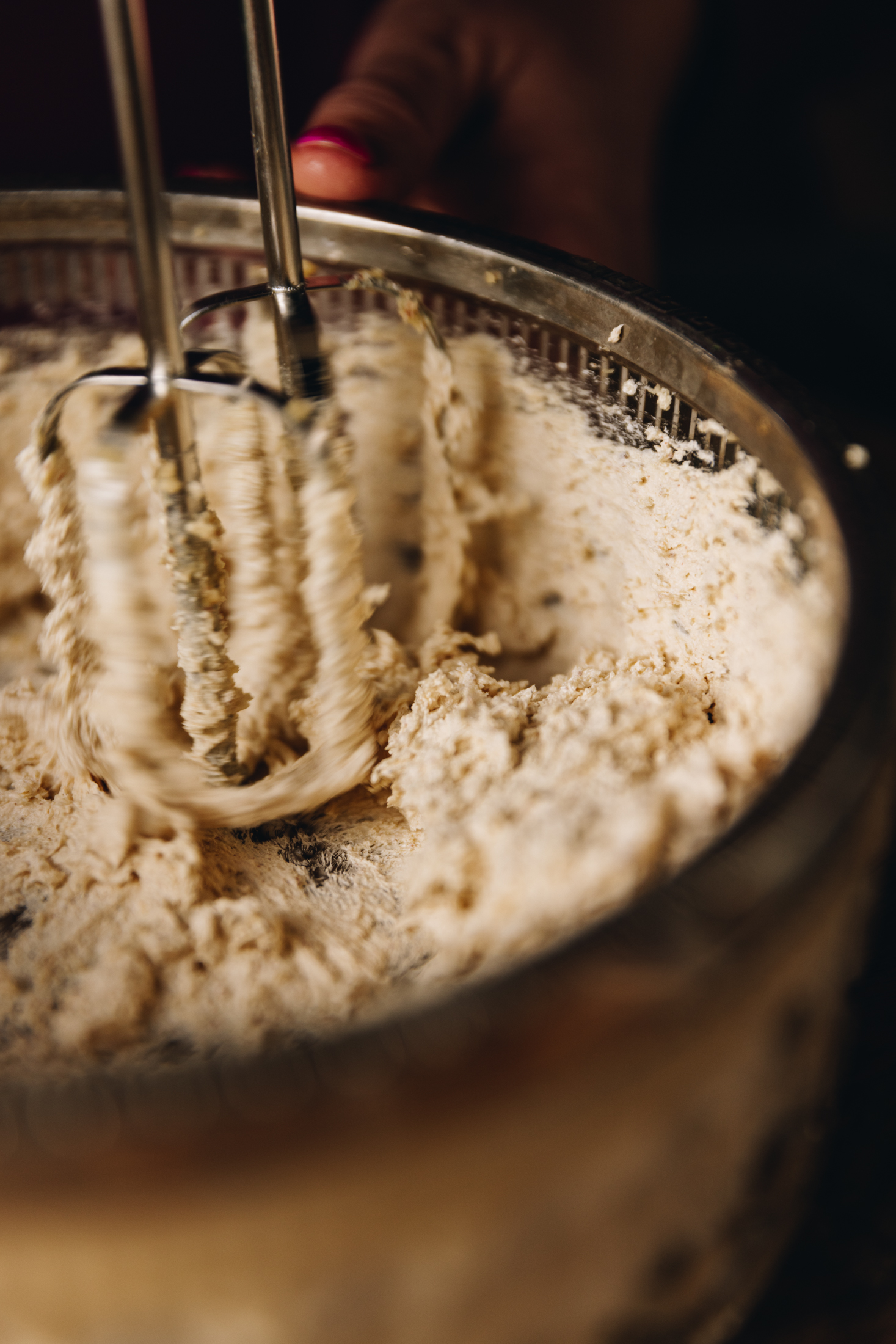 In a glass vintage bowl with silver trimming is whipped brown butter and sugar that is being whipped with hand beater whisk attachments. 