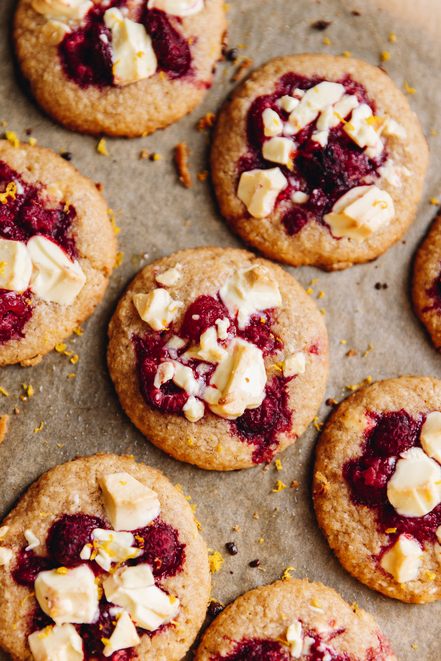 A top shot shows freshly baked white chocolate raspberry biscuits that are on brown baking paper. 