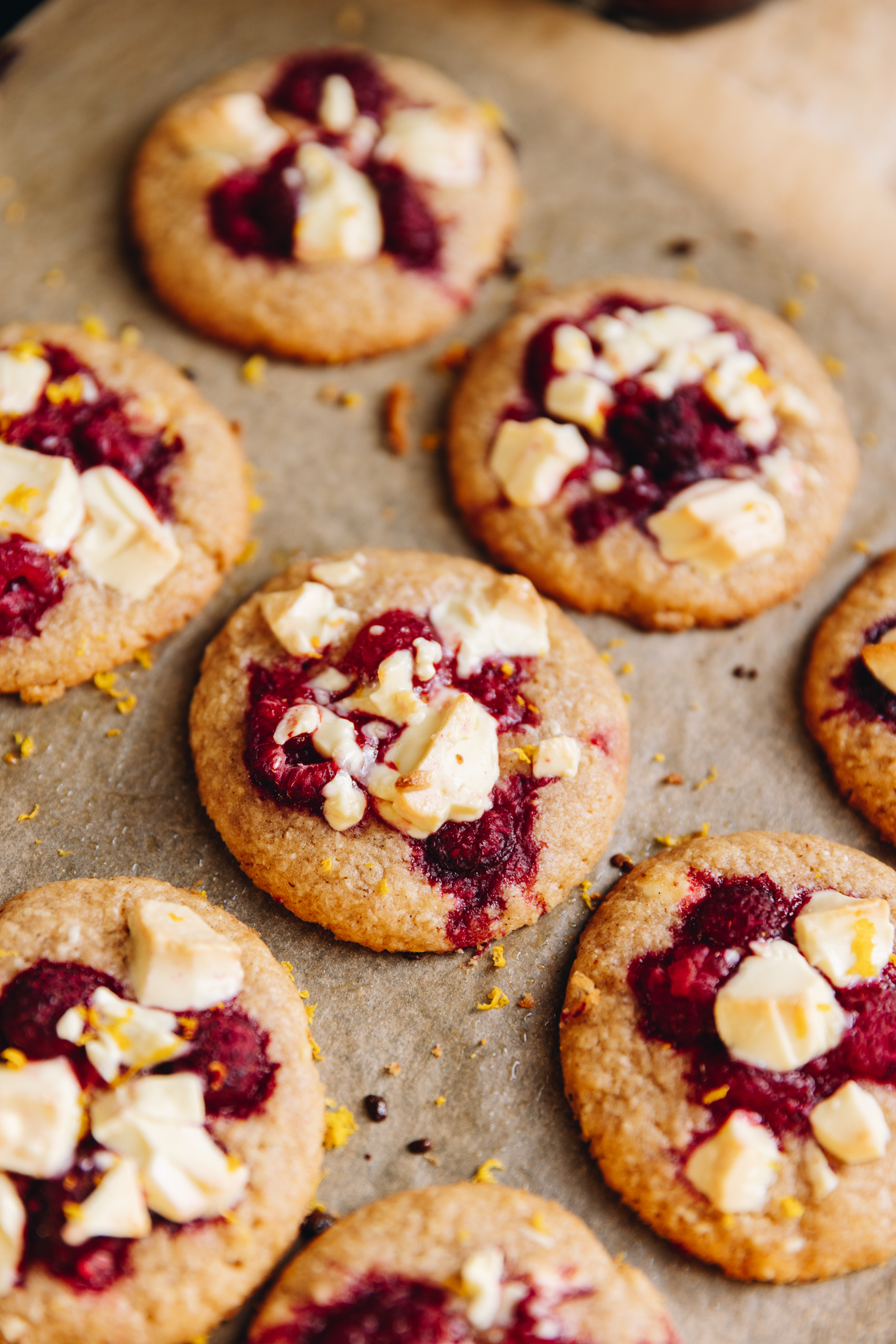 A top shot shows freshly baked white chocolate raspberry biscuits that are on brown baking paper.