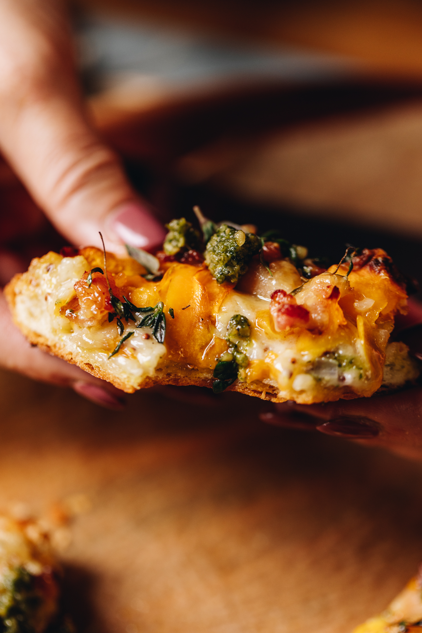 A mini creamy pumpkin tart is held in Naomi's hands to shows the baked tart with a crunchy pastry, pumpkin, bacon and green pesto on top. A bite has been taken out of the tart.