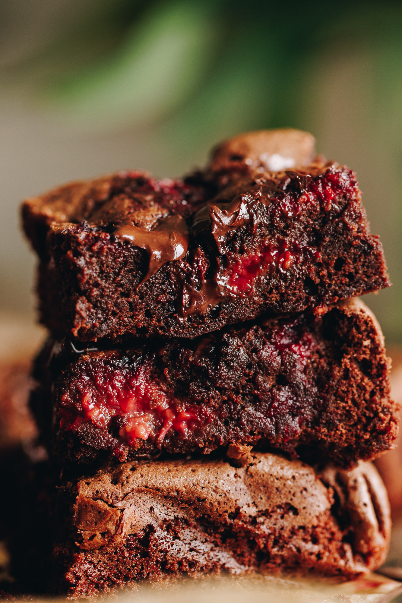Three pieces of chocolate and raspberry brownie are piled on top of each other revealing the raspberry and chocolate inside. 