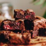 Slices of freshly baked Chocolate and Raspberry Brownie are piled on top of each other, sitting on brown baking paper.