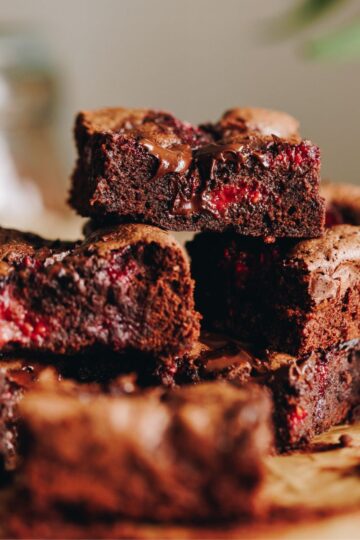 Slices of freshly baked Chocolate and Raspberry Brownie are piled on top of each other, sitting on brown baking paper.