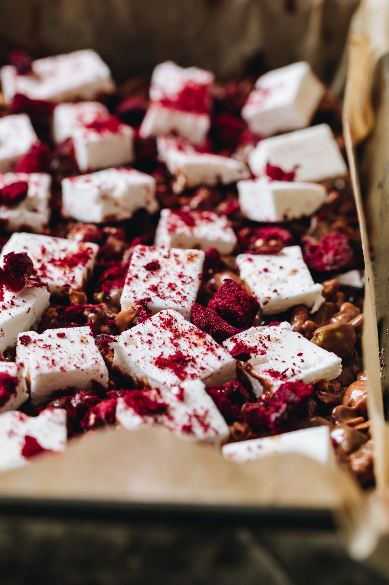 In a baking tray line d with baking paper is easy homemade vanilla marshmallow that has been cut in to squares and has freeze-dried plums sprinkled over top of it. 