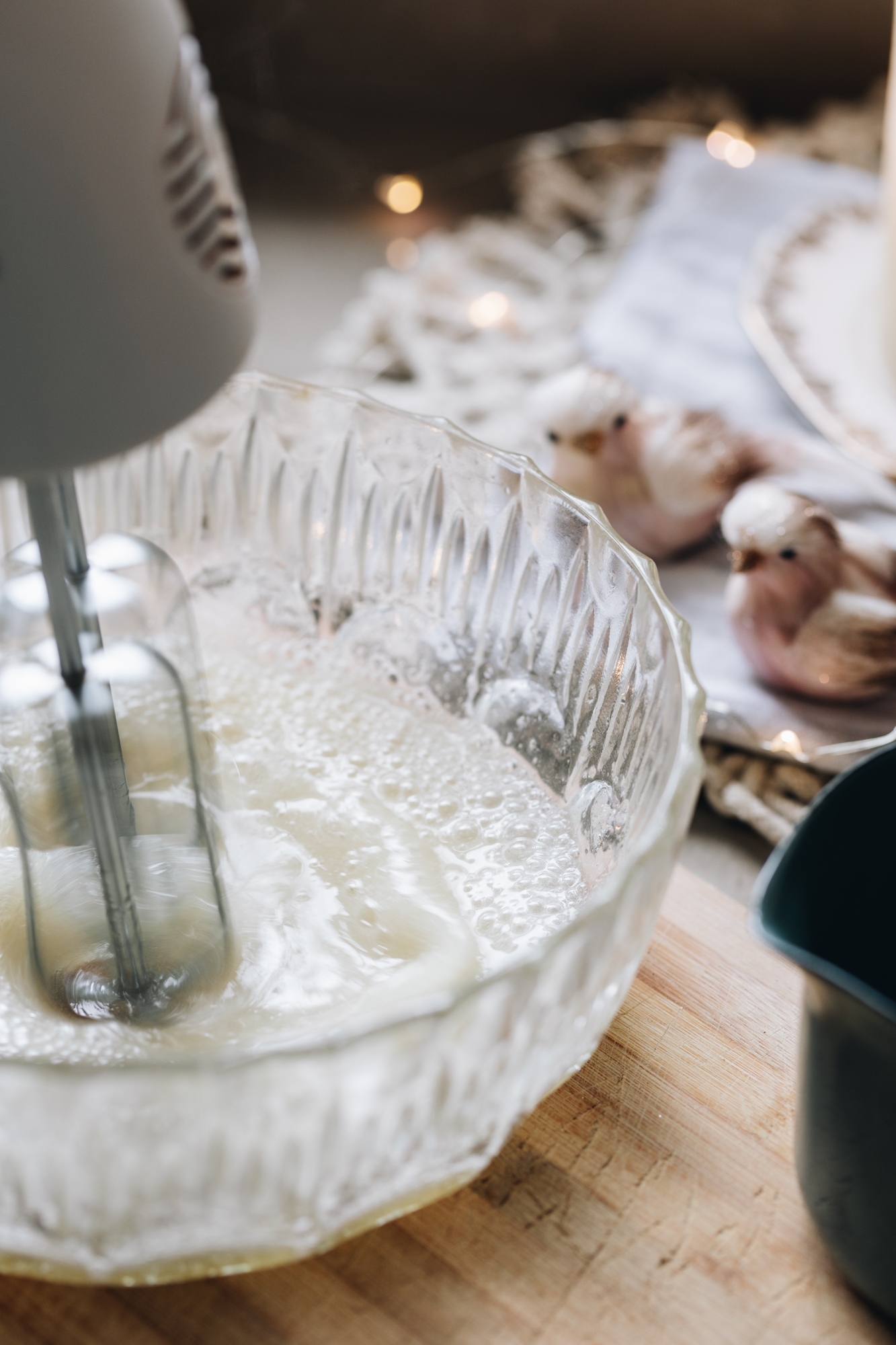 A glass vintage bowl sits on a wooden board with small ornament birds in the background. A blue pot is next to the bowl.