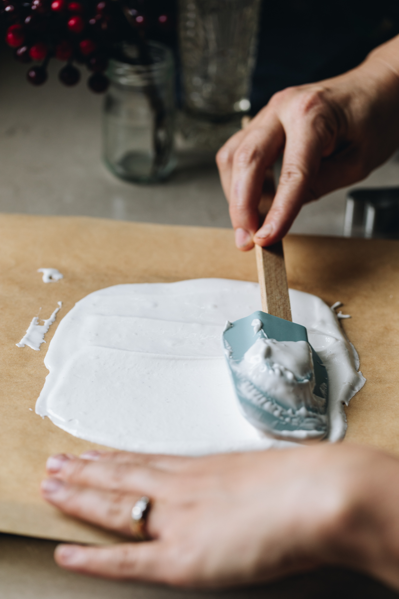 On brown baking paper is marshmallow being spread in a thin layer with a blue spatula with a wooden handle. 