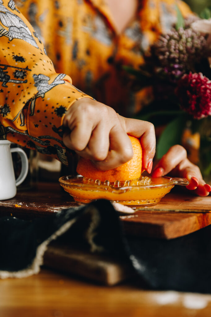 Fresh orange juice is being squeezed in to a glass juicer, it is on a wooden board. 