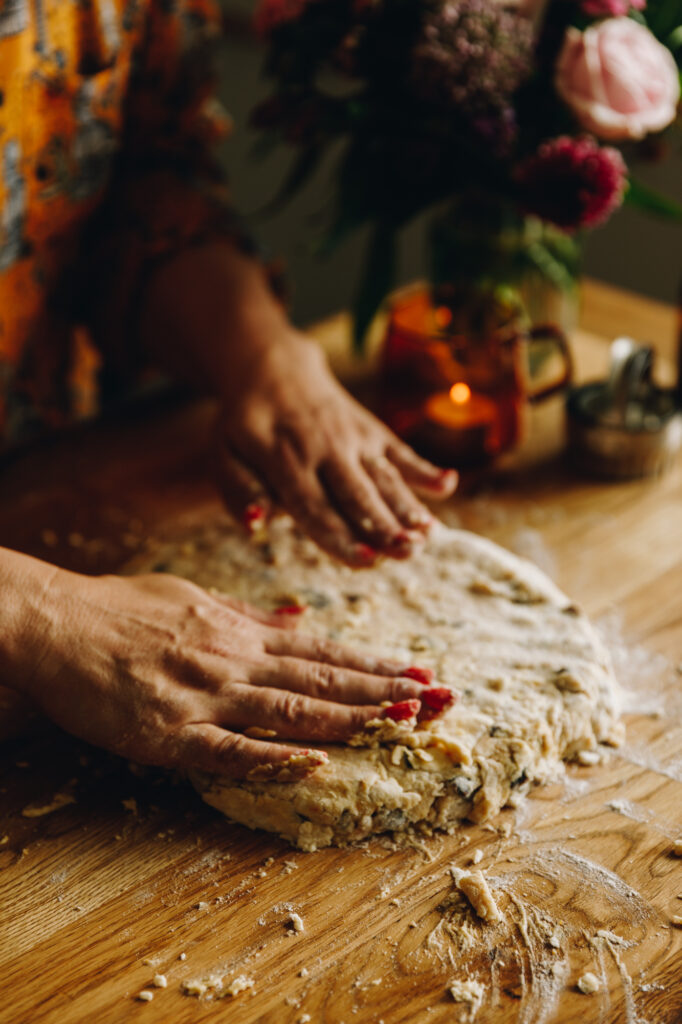 On a wooden table, Naomi Toilalo's hands are pressing the Date and Orange Scone dough in to a circle. 