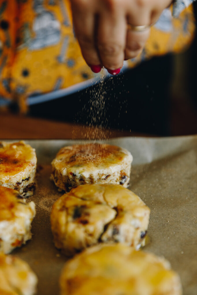 A close up shows the cinnamon sugar being sprinkled on top of the buttered Date and Orange Scones. 
