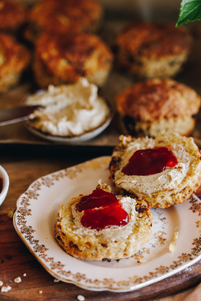 On a pink plate with a gold trim sits an Orange and Date Scone cut open with whipped brown butter and jam. 