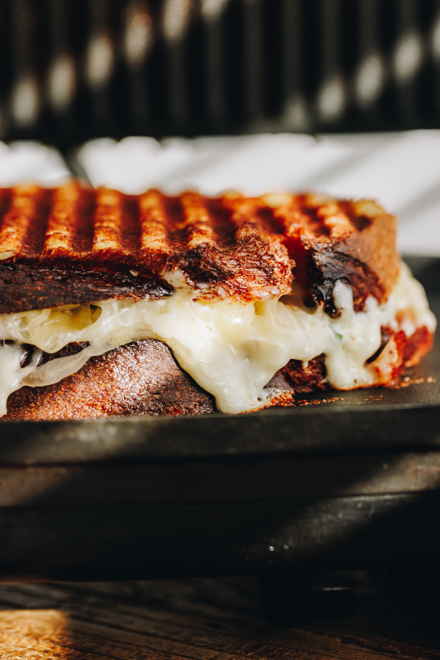 A freshly toasted maple bacon cheese toastie is sitting on a black toasted sandwich maker. It has grills marks on the top and cheese is oozing out of the middle.