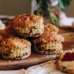 A pile of orange and date scones are freshly baked and are sitting on a gold tray on top of a wooden board.
