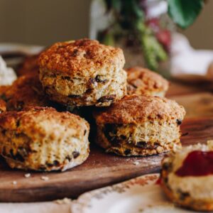 A pile of orange and date scones are freshly baked and are sitting on a gold tray on top of a wooden board.