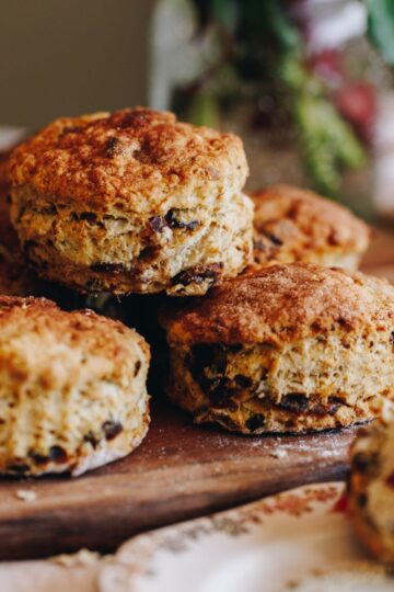 A pile of orange and date scones are freshly baked and are sitting on a gold tray on top of a wooden board.