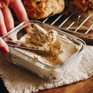 Whipped brown butter has been set in a small glass container, it is on a cream cloth with scones in the background.