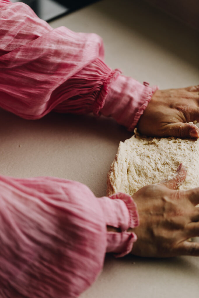 Two arms with pink puff sleeves are kneading a dough on a white bench for the Light and Fluffy Fry Bread.