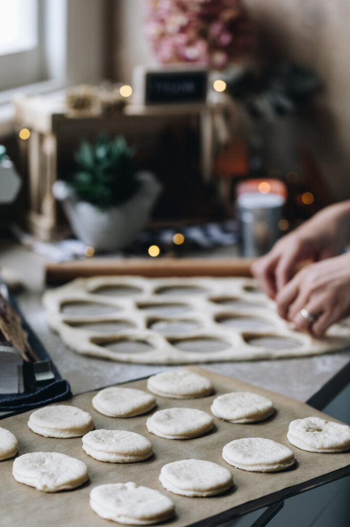 Pieces of Light and Fluffy Bread dough are placed on a tray, spaced out on brown baking paper. The dough behind it shows that the dough has been cut out with a round cutter. 