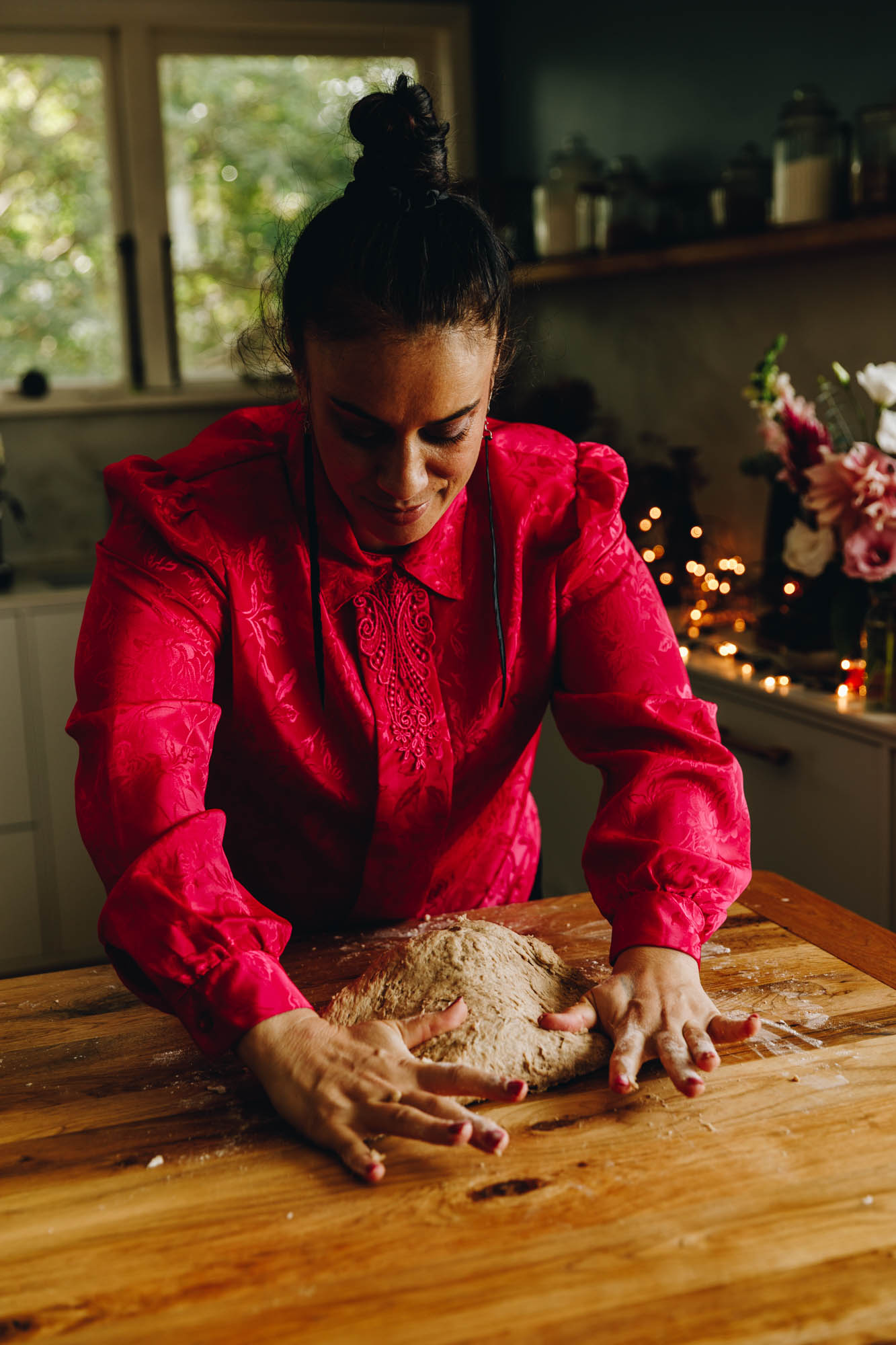 Naomi Toilalo is wearing a bright pink shirt and is kneading a spiced dough on a wooden table. 