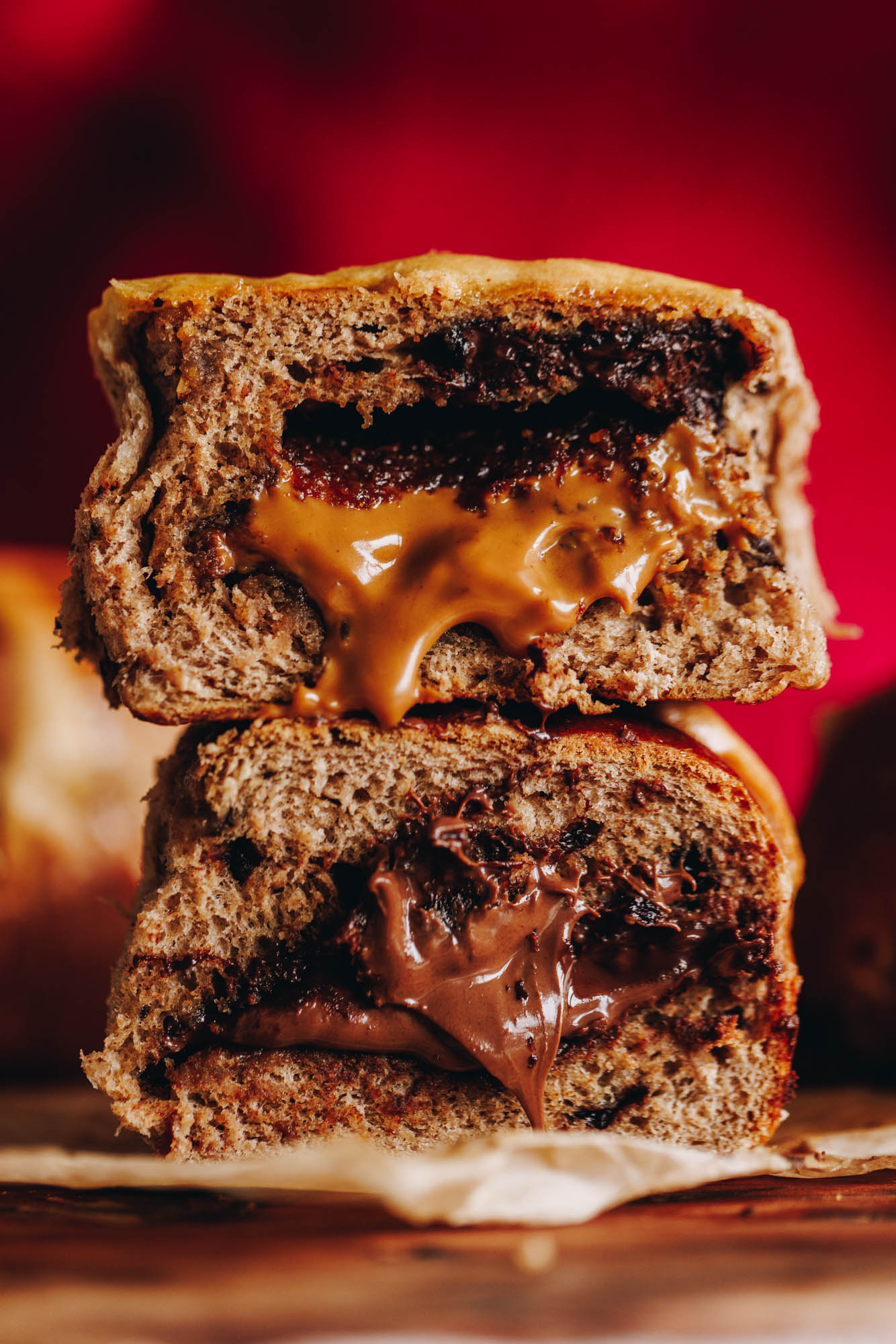 A baked Nutella hot cross bun is cut open to reveal the gooey Nutella centre. On top of the bun is a Biscoff bot cross bun with gooey biscoff coming out of it. 