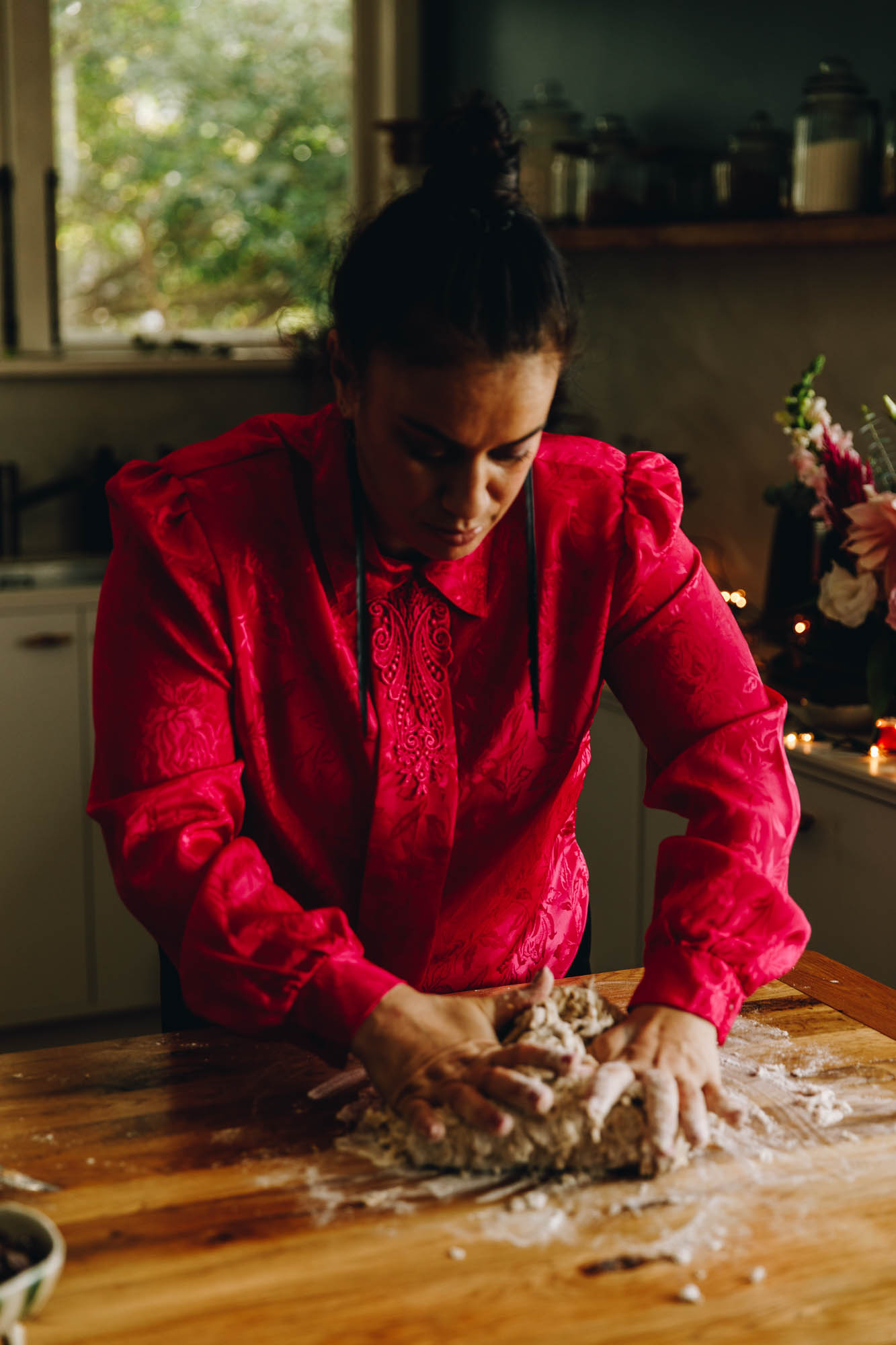 Naomi Toilalo is wearing a bright pink shirt and is kneading a spiced dough on a wooden table.