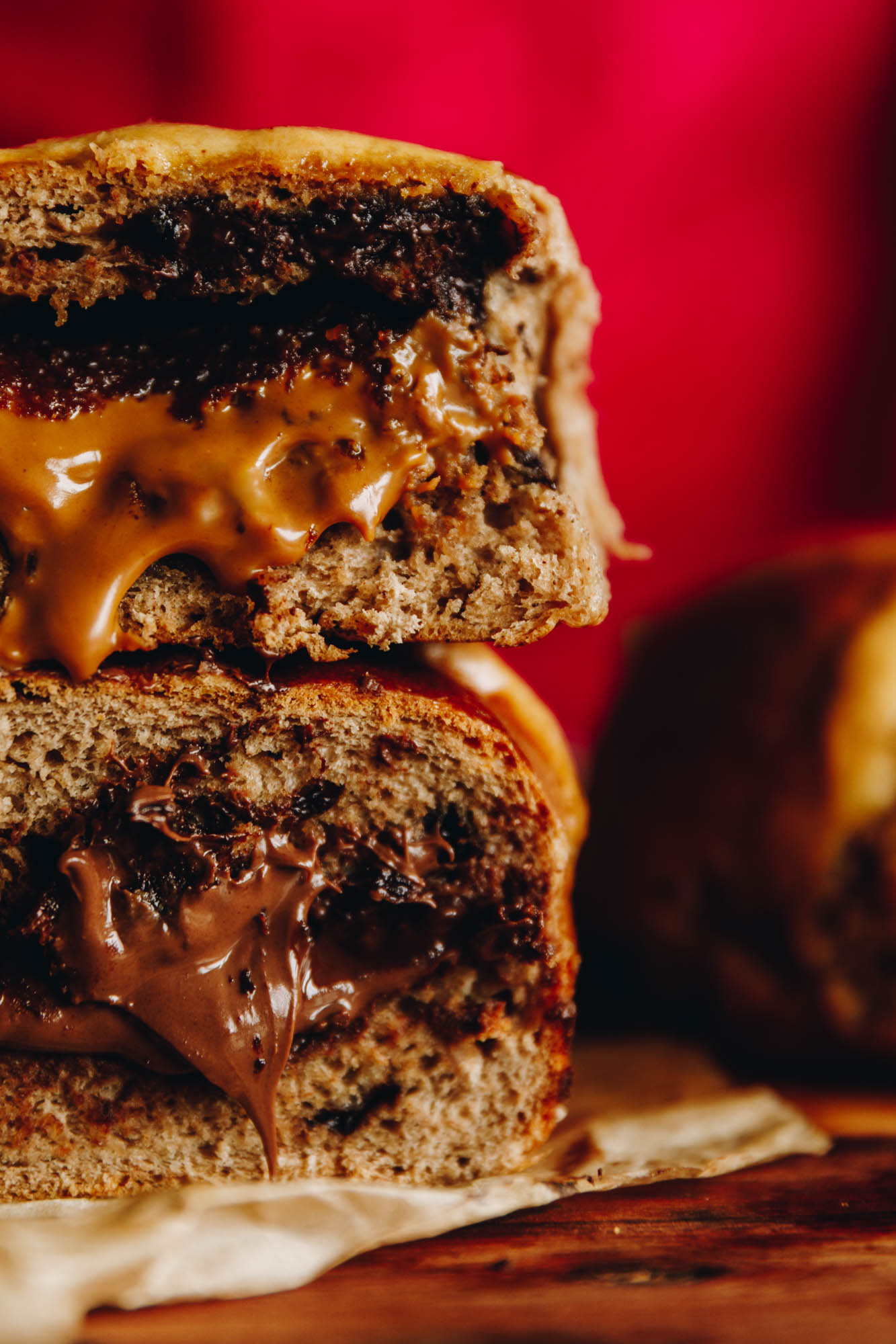 A baked Nutella hot cross bun is cut open to reveal the gooey Nutella centre. On top of the bun is a Biscoff bot cross bun with gooey biscoff coming out of it.