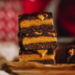 Close up shot of three pieces of No-bake Peanut Butter Slice piled on top of each other with a pink backdrop.