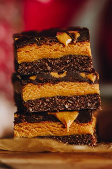 Close up shot of three pieces of No-bake Peanut Butter Slice piled on top of each other with a pink backdrop.