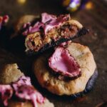 An easter egg cookie is on a wooden board, another cookie has been cut in half to reveal the gooey inside.