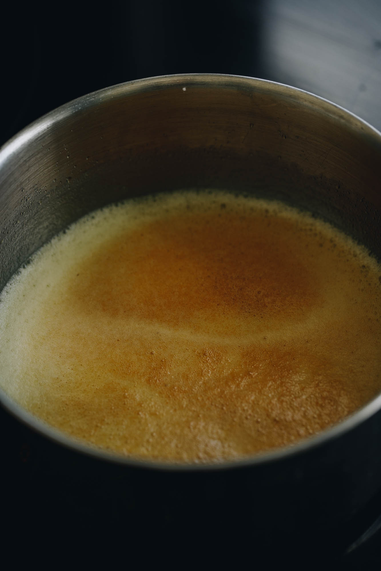 A shot shows a silver pot with brown butter foaming in it. In the centre are brown bits that have floated to the top.