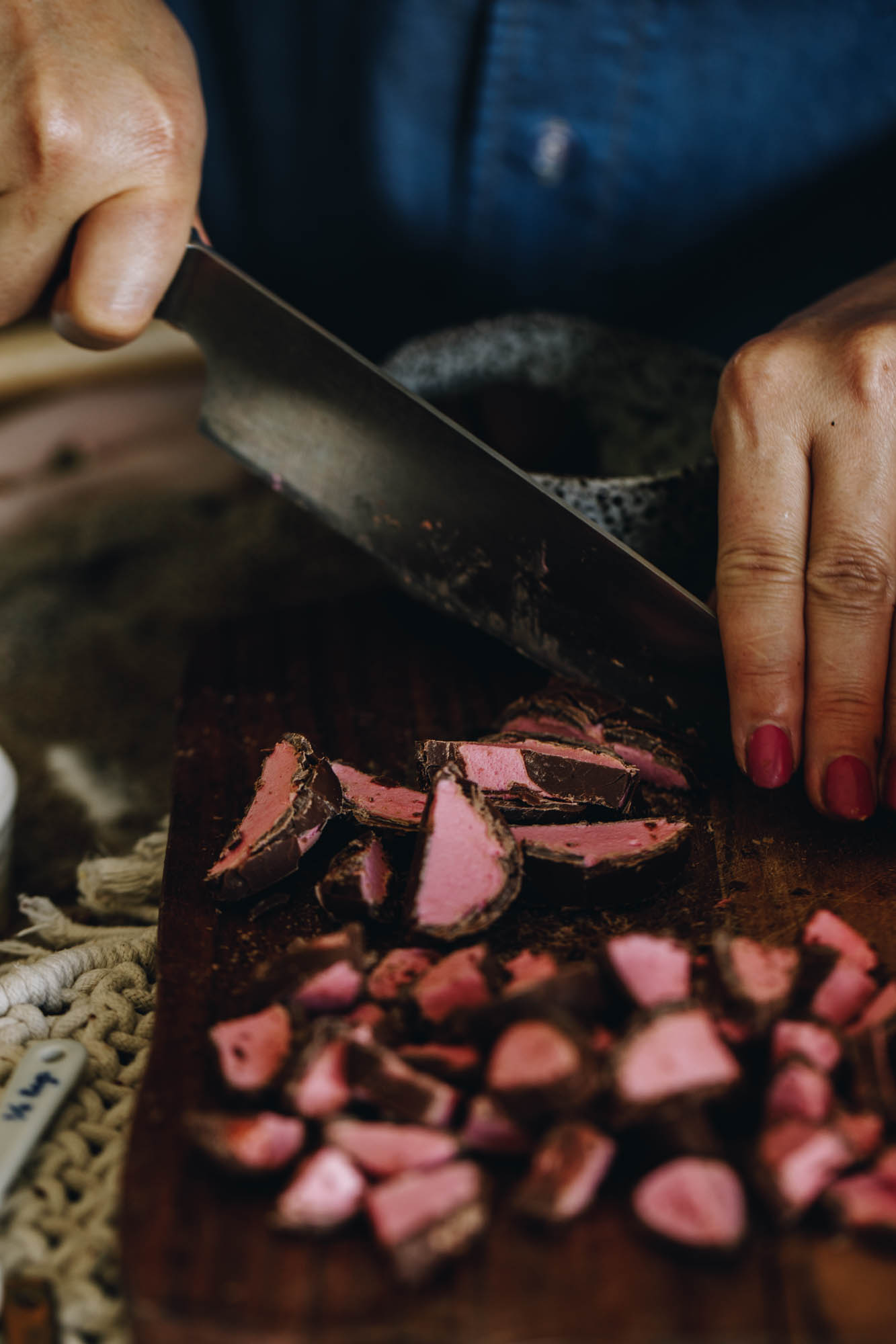 On a wooden chopping board is pink marshmallow chocolate easter eggs that have been sliced. Naomi is slicing through one with a large silver knife. 