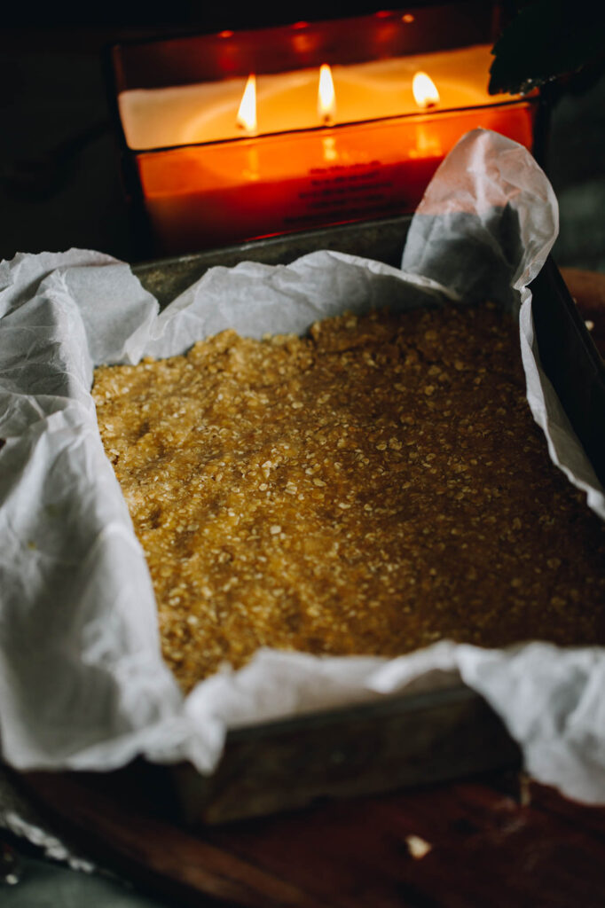 Best Oaty Caramel Slice unbaked base mixture, pressed in to the tin with a large candle in the background