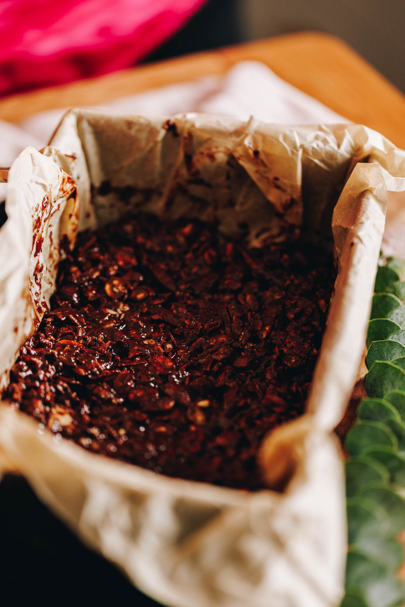 A tin lined with brown paper and the chocolate and seed mixture has been pressed in. It sits on a wooden table. 