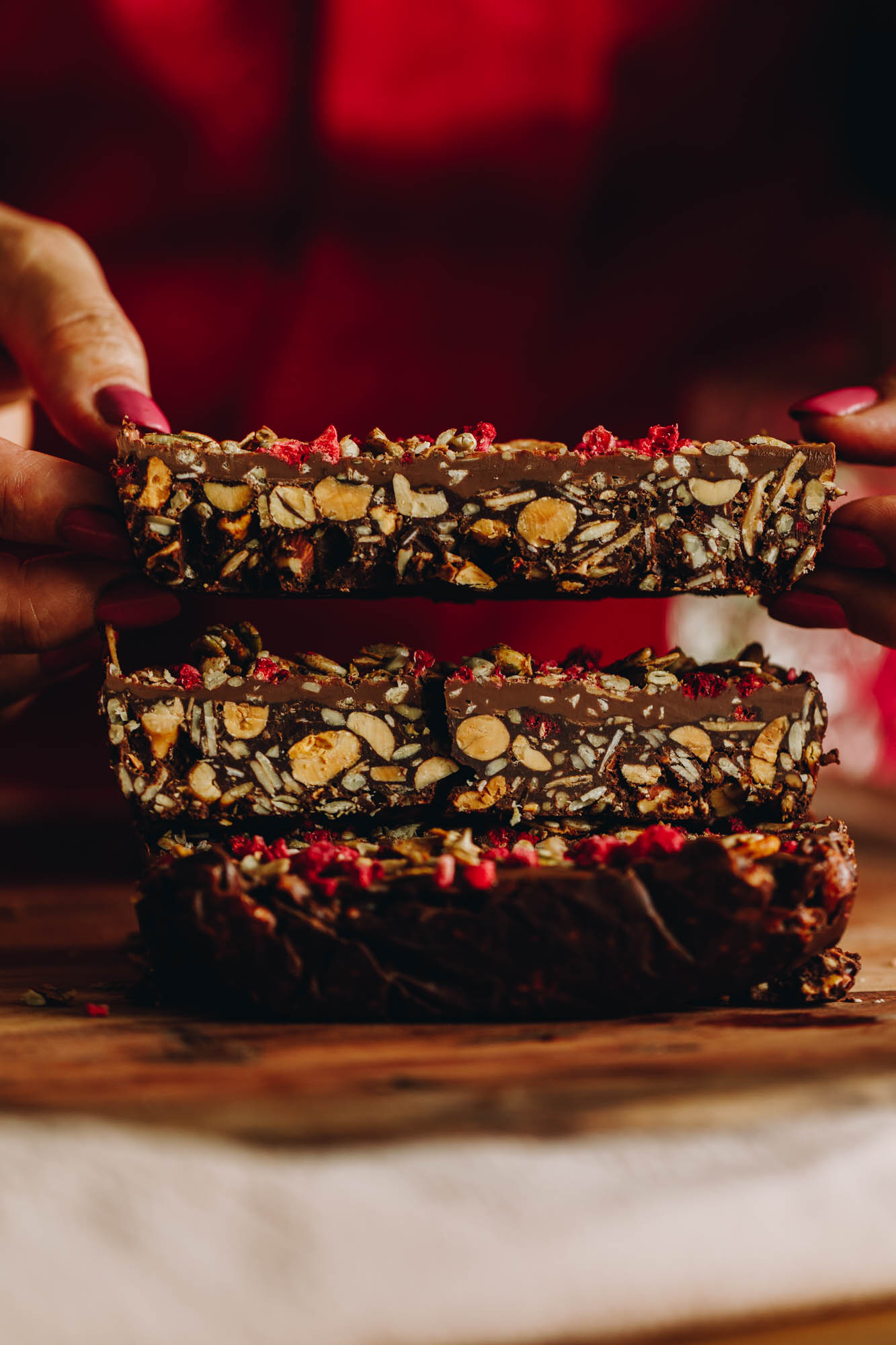 A pile of three slices of chocolate nut and seed slices. The texture shows all the nuts inside the bar. One piece is being held up by Naomi Toilalo. 