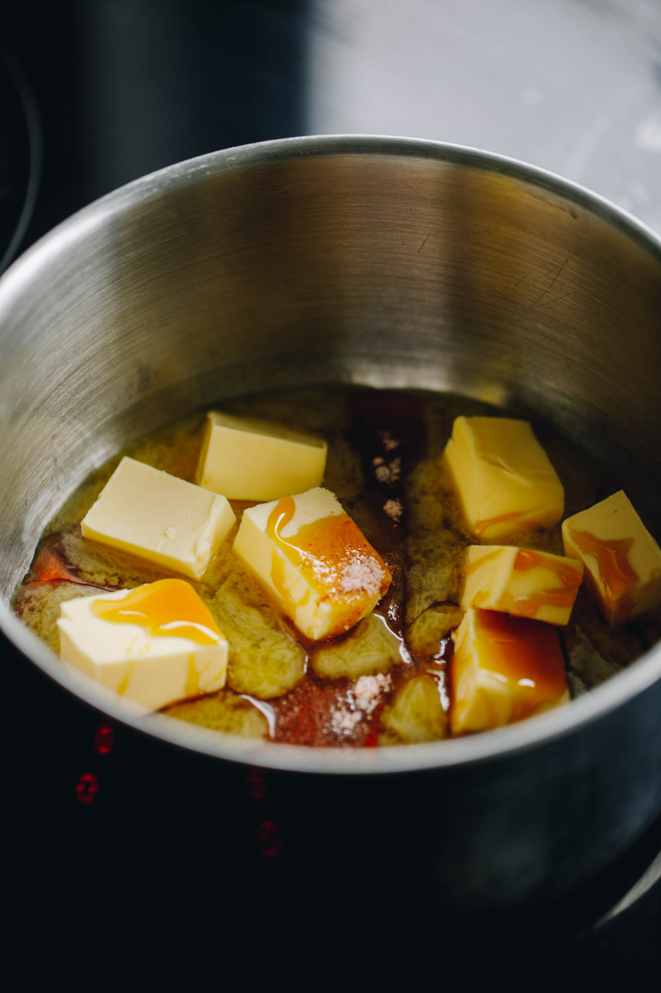 A silver pot sits over a black stove top. In the pot is butter and golden is syrup that has started to melt. 