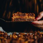 Close up of the Best Oaty Caramel Slice being held by a serving knife and a hand.