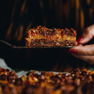 Close up of the Best Oaty Caramel Slice being held by a serving knife and a hand.