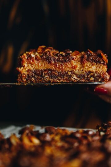 Close up of the Best Oaty Caramel Slice being held by a serving knife and a hand.