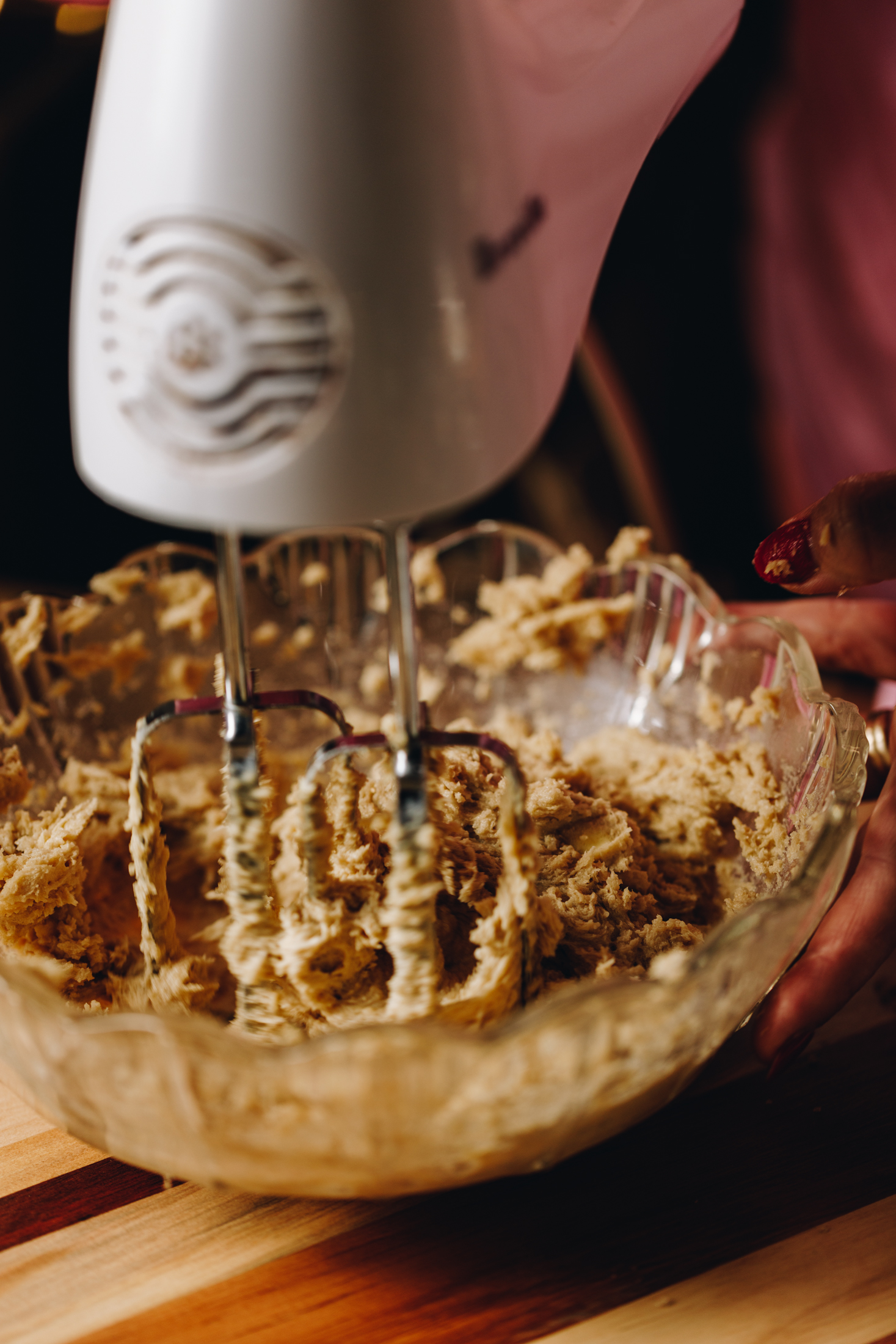 Close up of butter and sugar being whipped in a vintage bowl on a wooden board. It is being whipped with a hand mixer.