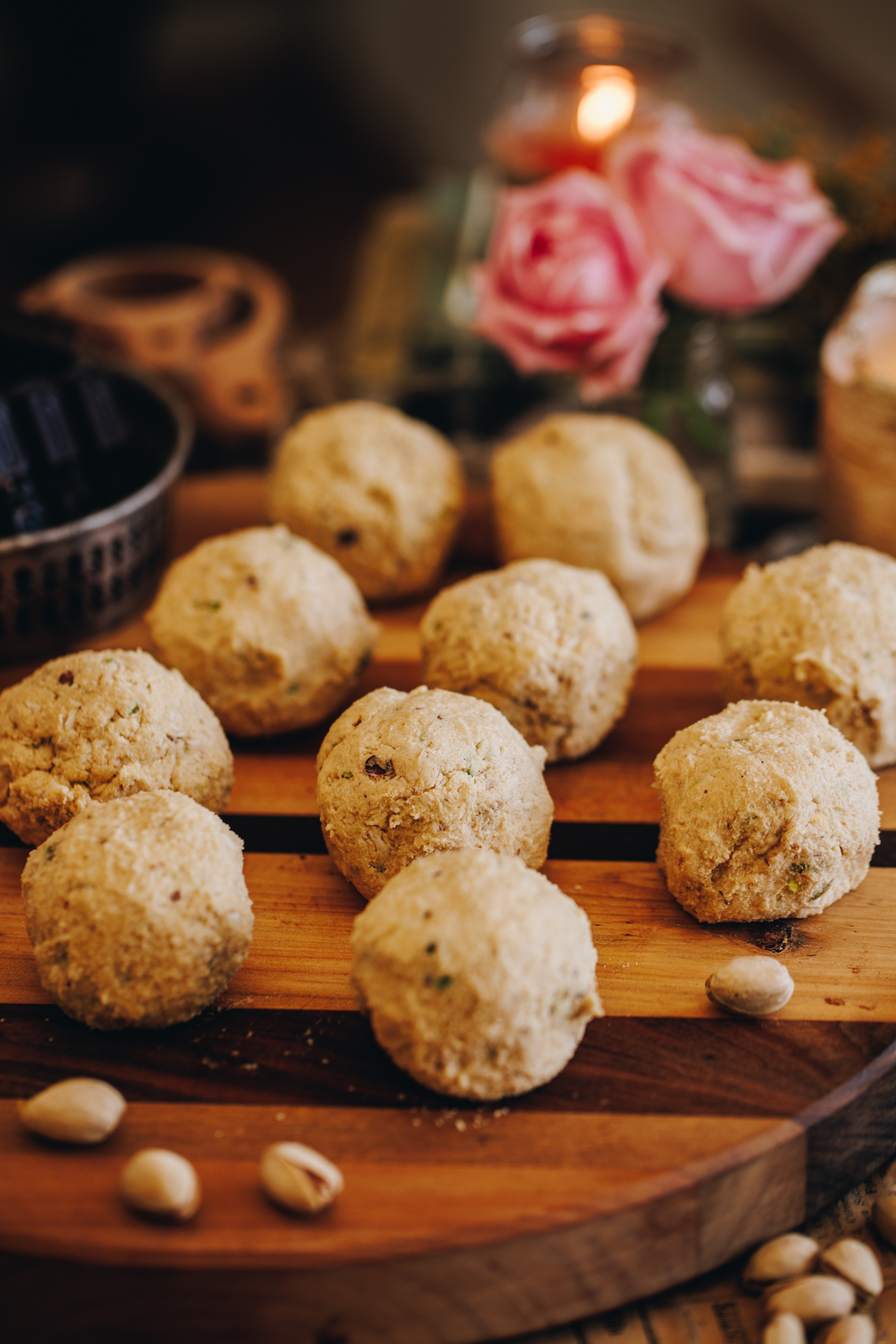 On a wooden board is the pistachio and chocolate biscuit dough rolled in to balls. 