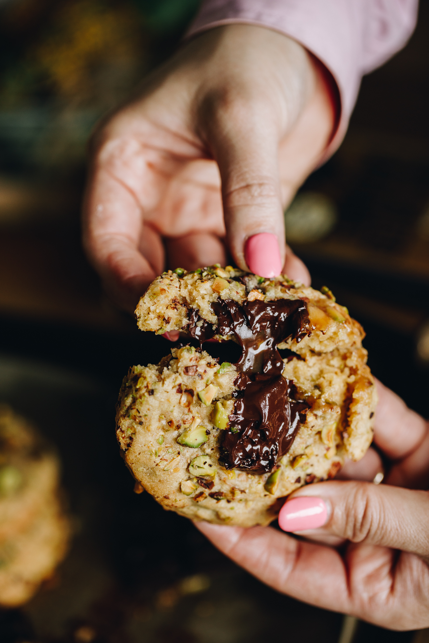 Close shot of a pistachio and chocolate cookie that is being opened up to reveal the gooey chocolate centre. 