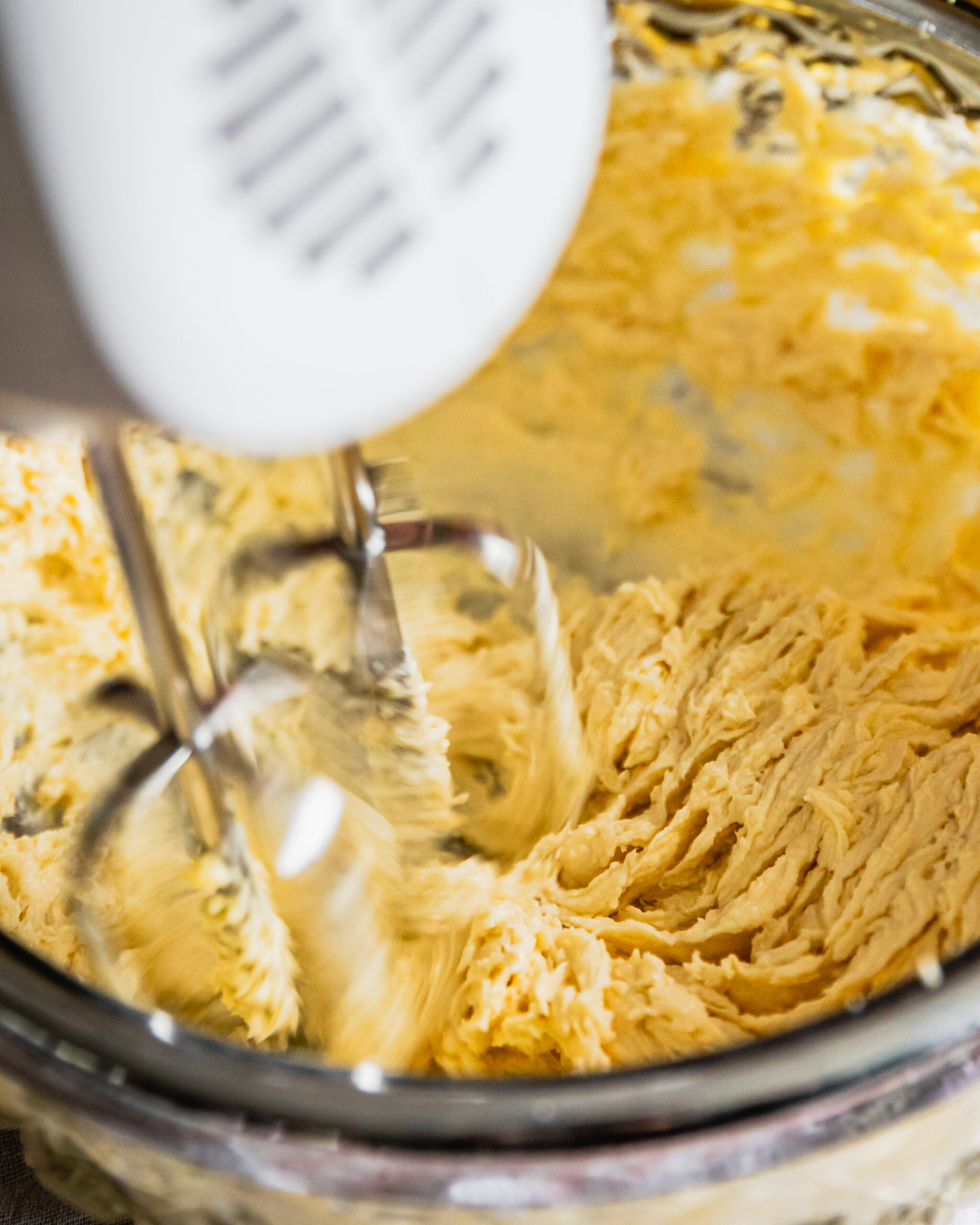 A close of the butter and sugar being whipped together in a glass bowl that is sitting on a wooden board.