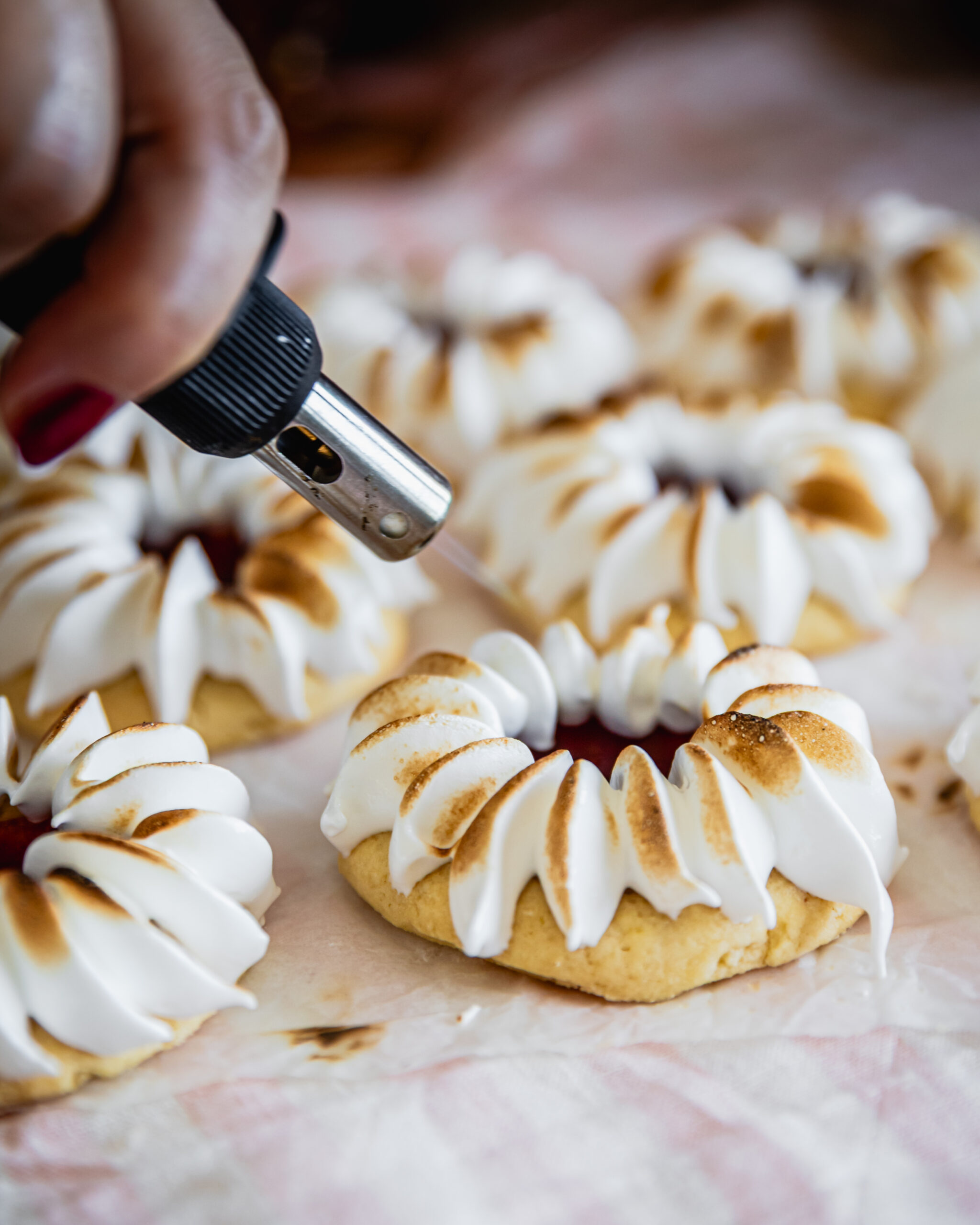 Close up of strawberry jam drops as the meringue on top is being torched. They are on white baking paper.