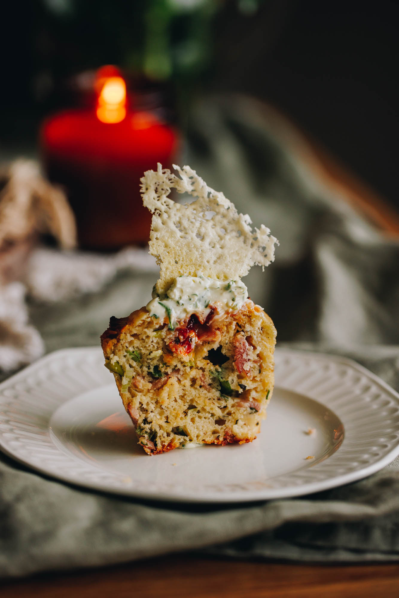 A Cheesy Bacon Savoury Muffin is cut open on a plate revealing the inside with tomato chutney at the top, a cream cheese topping and a paramsen wafer on top. 