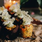 Freshly baked cheesy bacon savoury muffins are sitting on a cooling rack. One of the muffins has no case showing the whole muffin with cream cheese topping and a parmesan crisp on top.