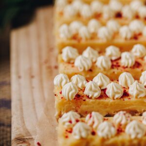 White chocolate yogurt cream piped on to lemon bars with a sprinkle of freeze dried raspberries on top.