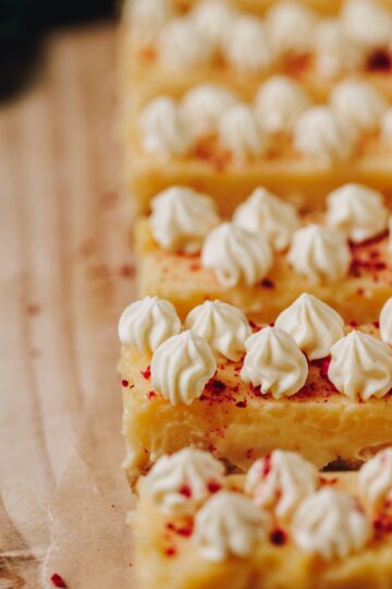 White chocolate yogurt cream piped on to lemon bars with a sprinkle of freeze dried raspberries on top.