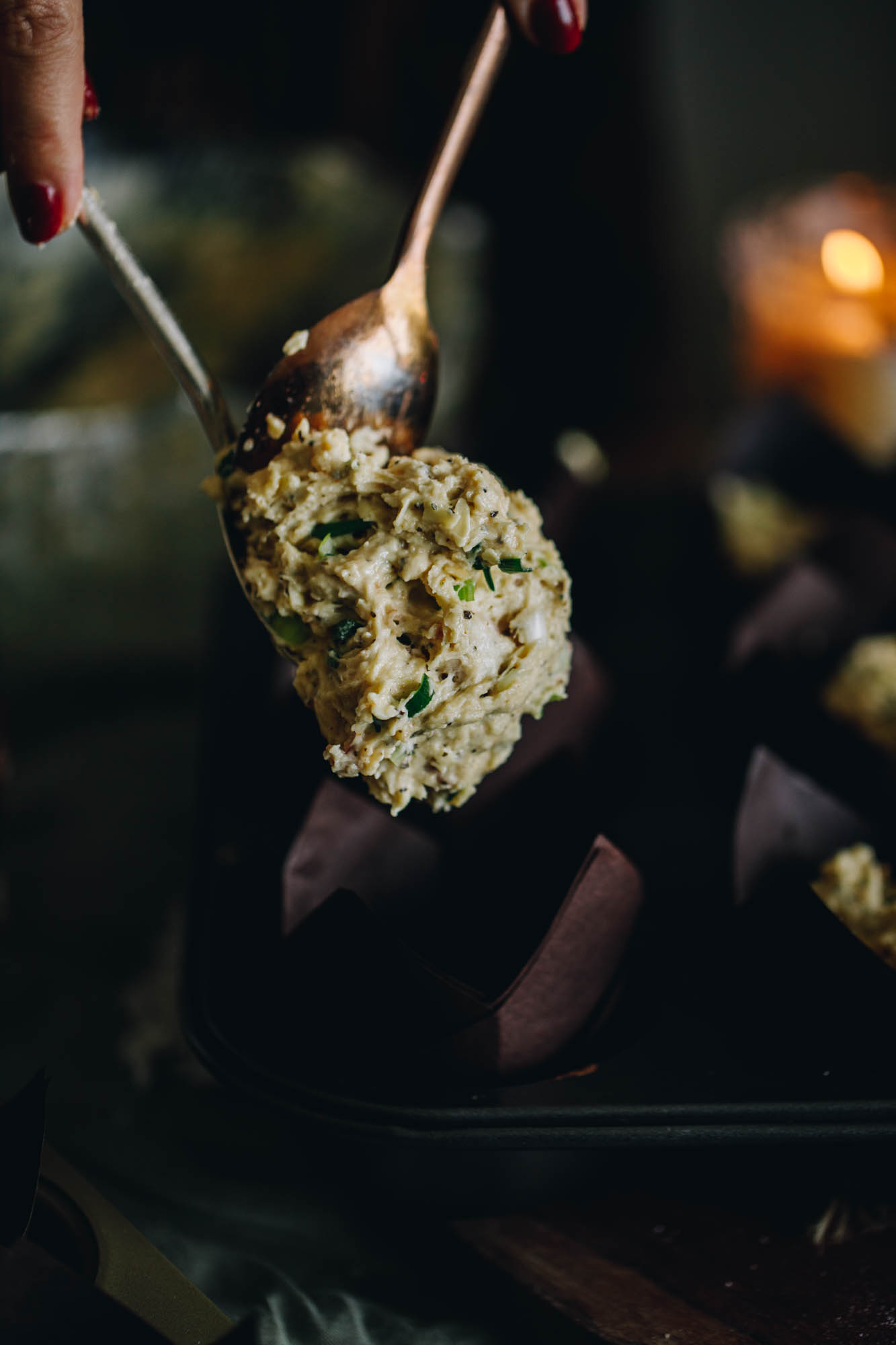 A spoon is adding a large spoonful of raw cheesy bacon savoury muffin mixture in to a brown muffin case.