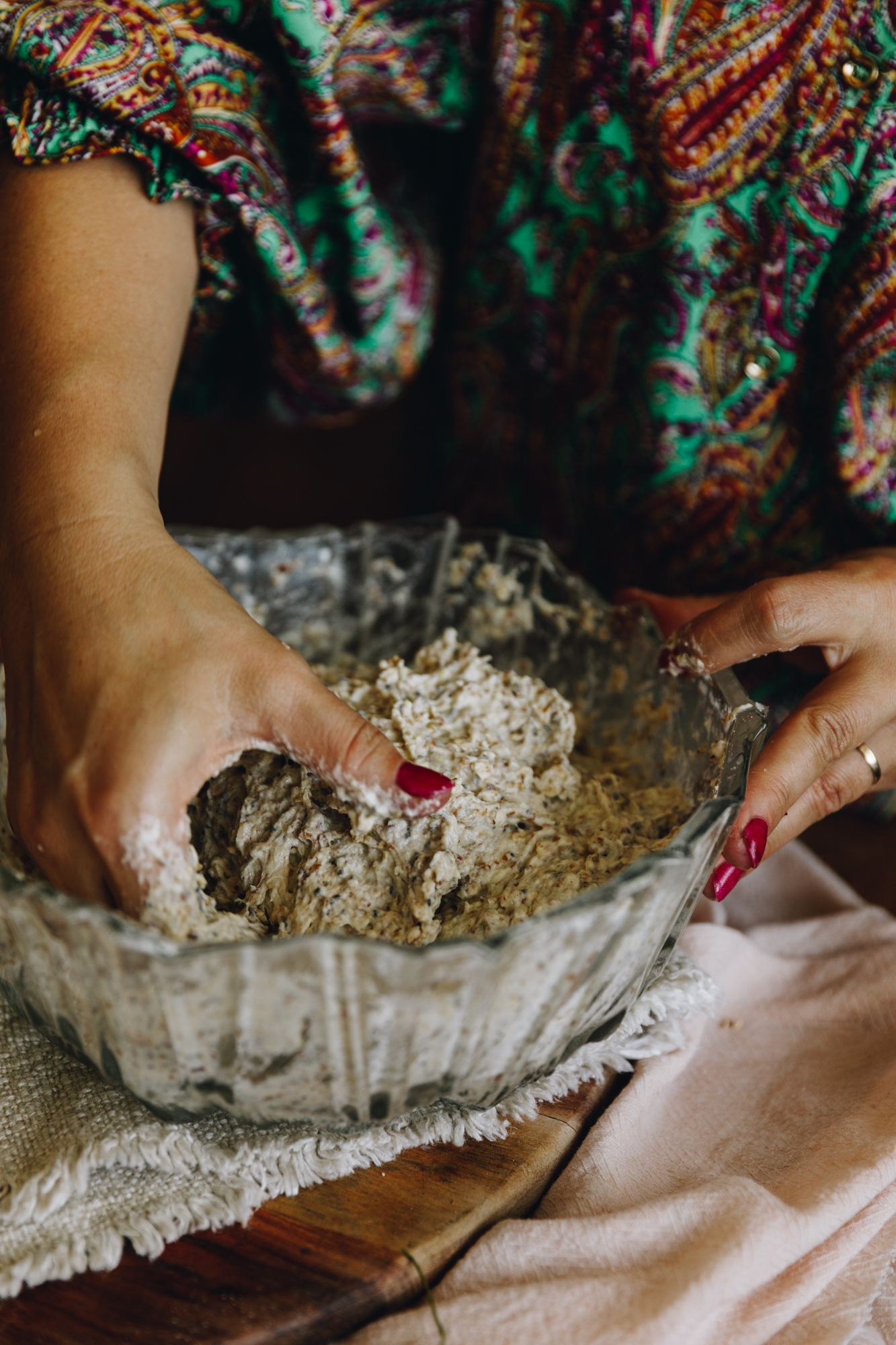 A hand with a colourful jumpsuit is gathering  the dough of the no-seeded oat bread beginning to stretch and fold the dough. 