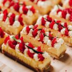 Close up of decorated lemon bars with piped cream, raspberries and lime leaf.