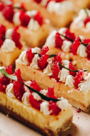 Close up of decorated lemon bars with piped cream, raspberries and lime leaf.